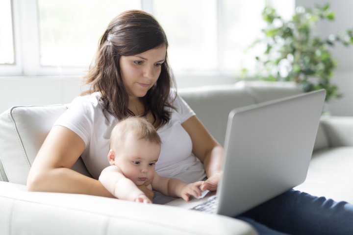 Junge Mutter mit Baby sitzt auf der Couch und chattet mit TeleHebamme