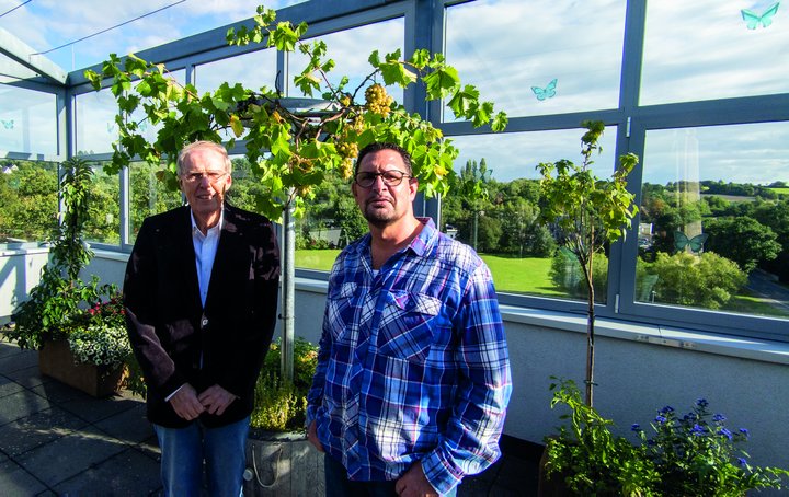 Zwei Männer lächeln auf der Dachterrasse in die Kamera