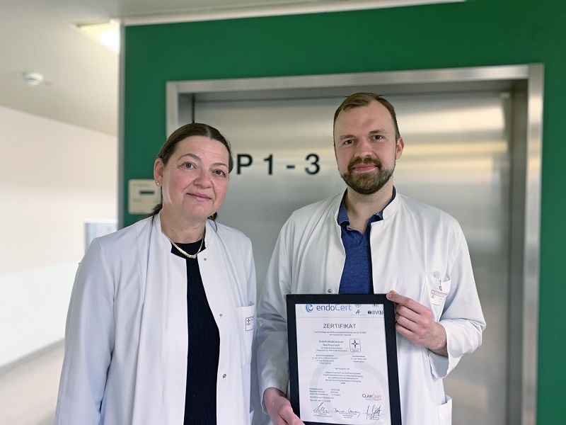 Frau und Mann in Arztkitteln halten Urkunde in der Hand