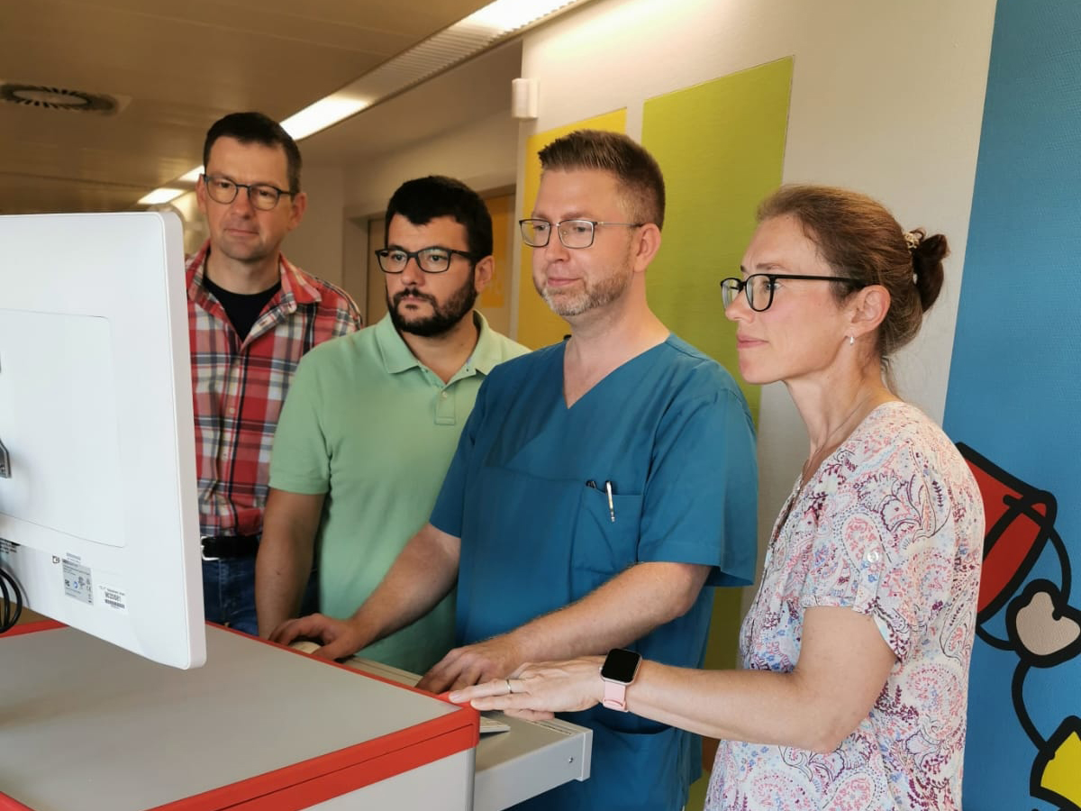 Vier Mitarbeiter stehen im Krankenhaus an einem Visitenwagen und prüfen die elektronische Patientenakte