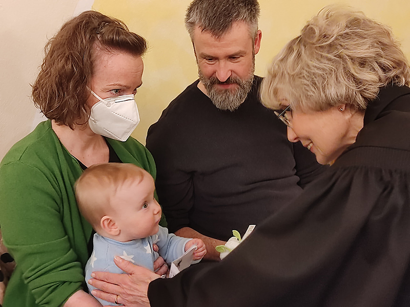 Pfarrerin segnet Baby, das auf dem Schoß der Mutter sitzt